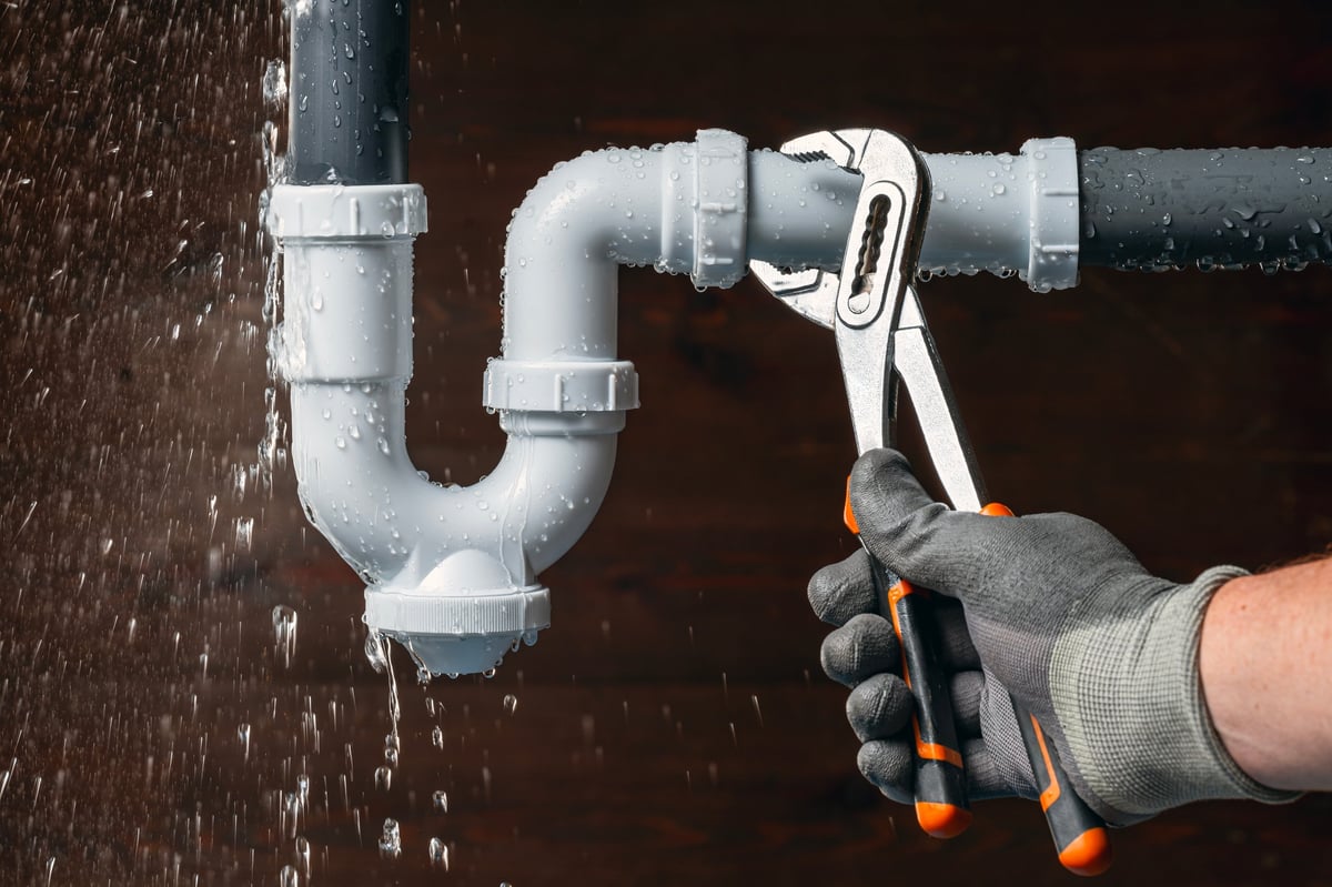 Plumber repairing a water leak in a sink drain pipe with adjustable pliers
